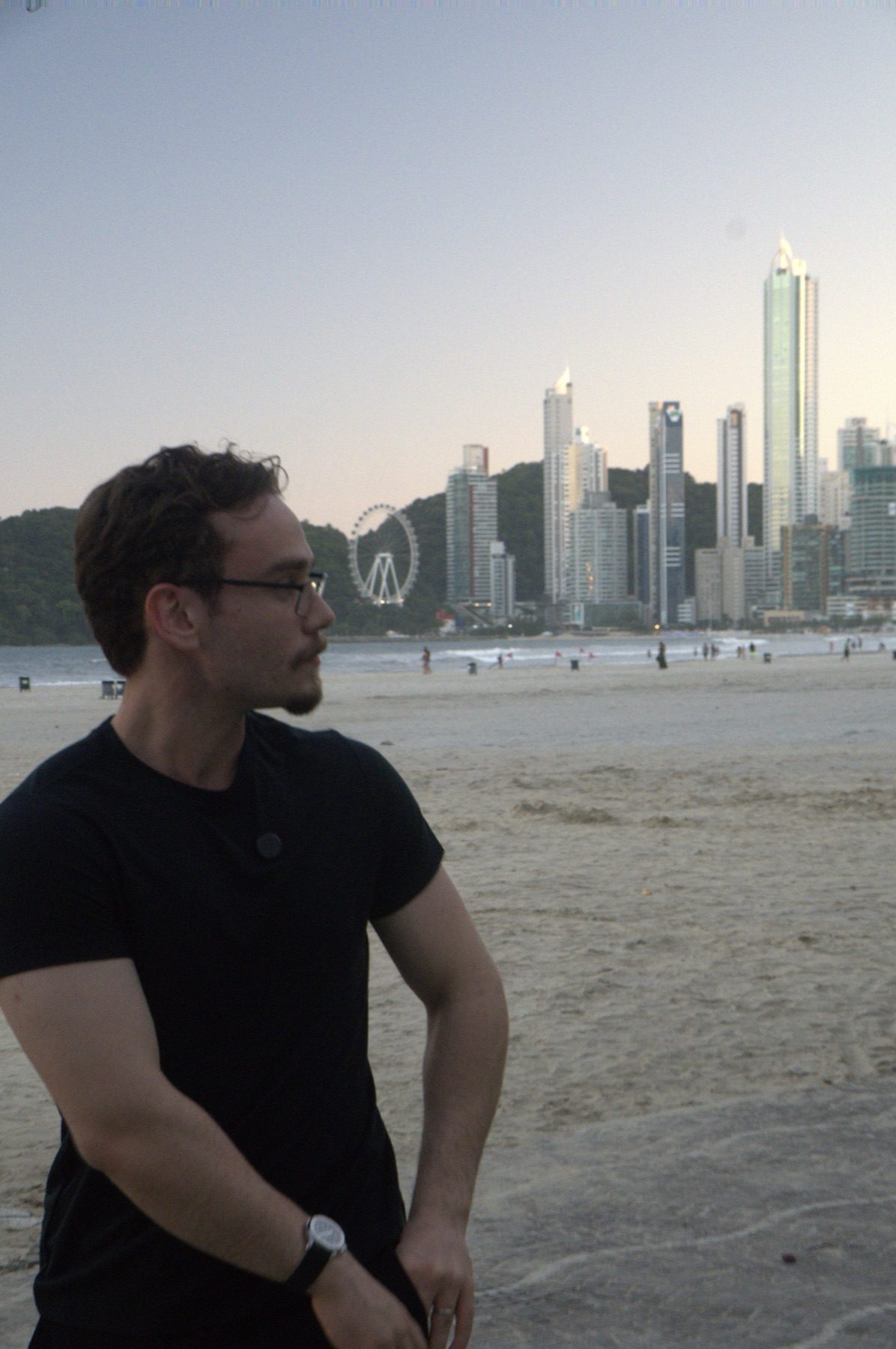 Hugo Petrakis na praia com a orla ao fundo no fim da tarde