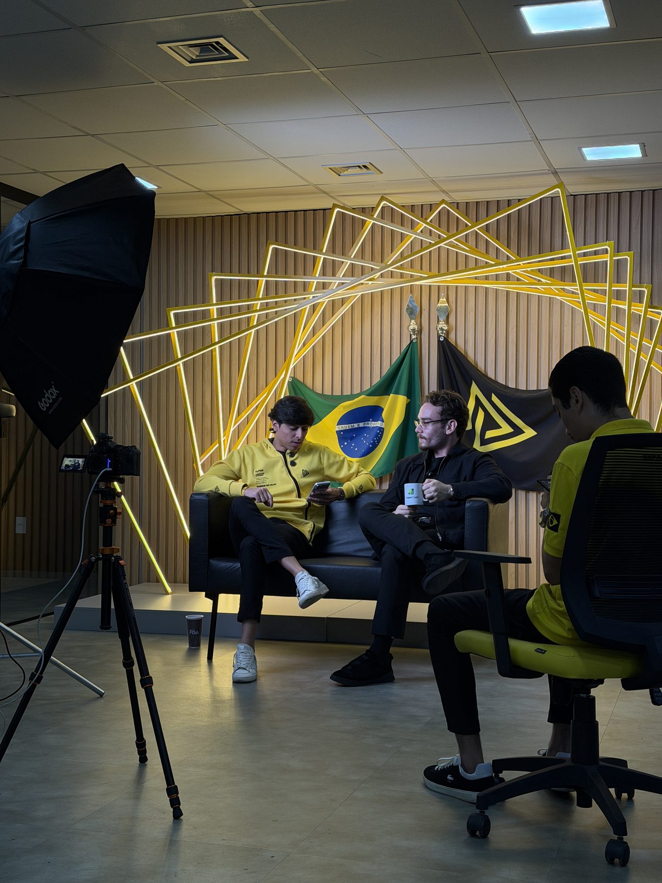 Set de gravação com luz, câmera e duas pessoas conversando no sofá