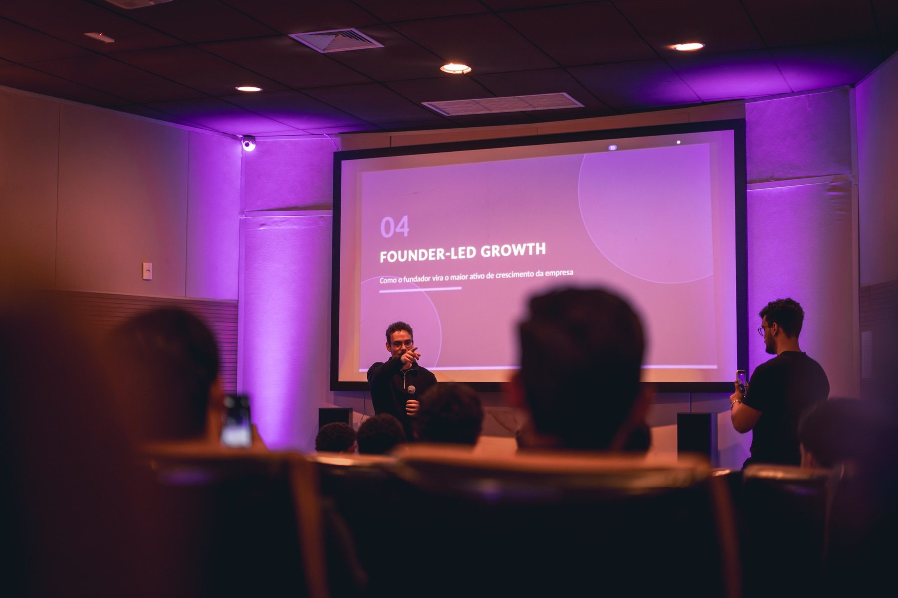 Hugo Petrakis no palco com microfone diante de uma plateia